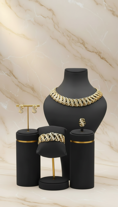 A jewelry set displayed on black mannequin stands against a beige marble background. The set includes a wide gold chain necklace on the largest stand, a matching chain bracelet on a smaller stand, a small gold ring on a cylindrical holder, and a pair of gold stud earrings on a slim gold T-stand.