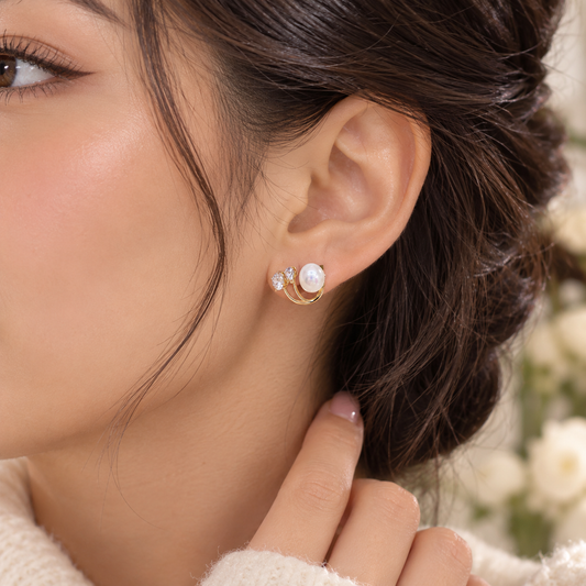 Close-up of a model wearing a gold-tone earring with a pearl-style bead and clear sparkling stones.

