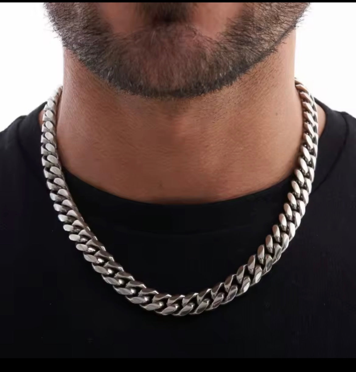 A close-up of a man's neck and lower face wearing a thick, polished silver Cuban link chain necklace over a black t-shirt.