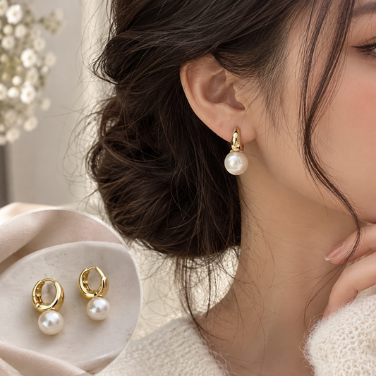 A close-up lifestyle shot of a woman wearing a gold hoop earring with a single white pearl drop, with a matching pair displayed on a beige fabric surface in the lower left.