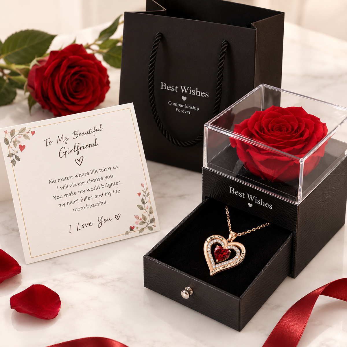 A romantic gift set featuring a red rose preserved in a clear display box with a heart-shaped gold pendant, a black gift bag, and a printed message card on a white marble surface.