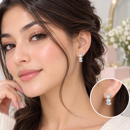 A close-up of a woman wearing a pair of silver-toned dangle earrings with clear stones, shown alongside a circular inset detail of the earring. The background is a soft, blurred indoor setting.