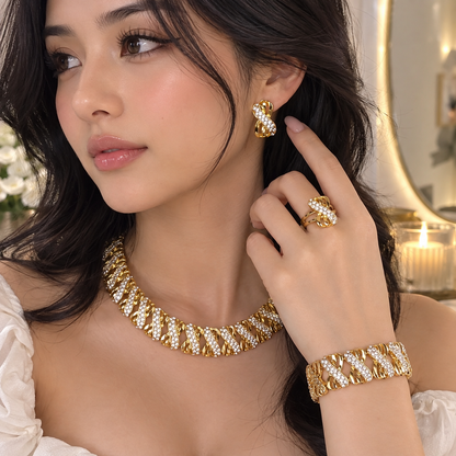 A woman models a gold jewelry set featuring a textured chain necklace, matching ring, bracelet, and earring with clear stones, set against a softly blurred indoor background.