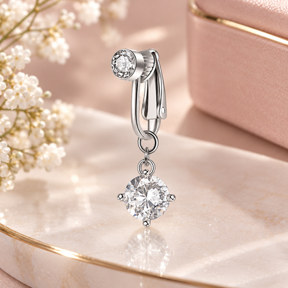 A silver-toned drop hoop earring with a large round clear gemstone dangle, styled on a pink marble surface with white baby's breath flowers and a soft pink jewelry box in the background.