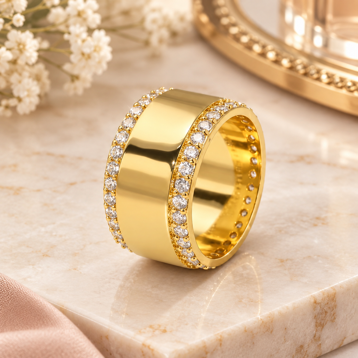 A wide yellow gold ring with pavé-set clear stones on both sides, centered on a light beige marble  surface.