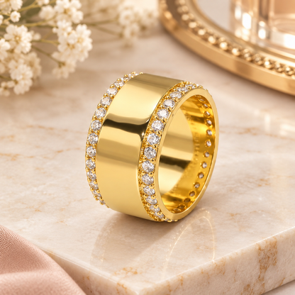 A wide yellow gold ring with pavé-set clear stones on both sides, centered on a light beige marble  surface.