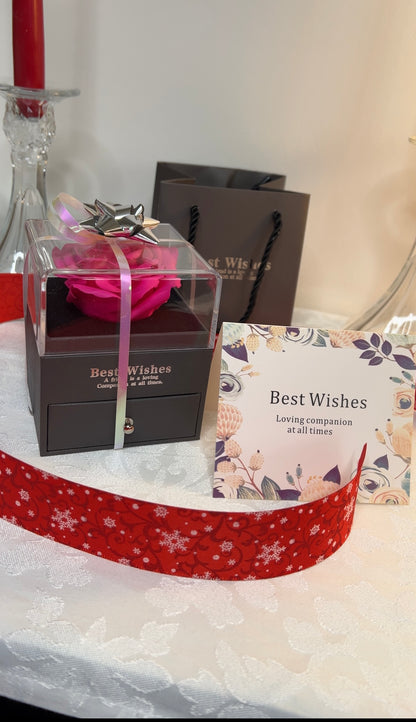 Gift box with pink rose, 'Best Wishes' card, and red ribbon on a white surface
