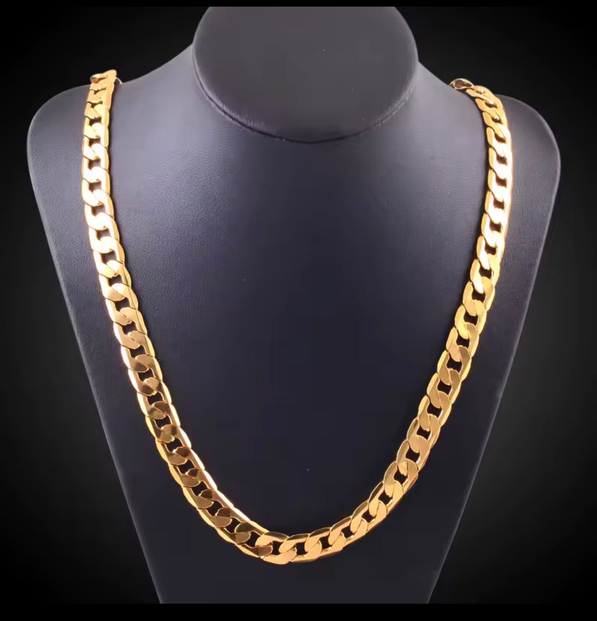 A thick gold Cuban link chain necklace displayed on a  black jewerly stand   on a black backgront.