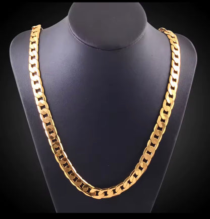 A thick gold Cuban link chain necklace displayed on a  black jewerly stand   on a black backgront.