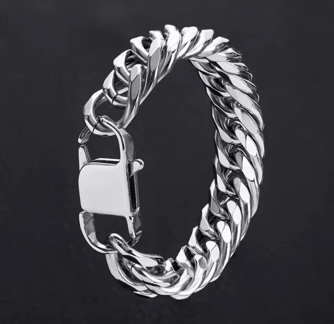 A chunky silver Cuban link chain bracelet with a polished clasp, shown on a dark black background.