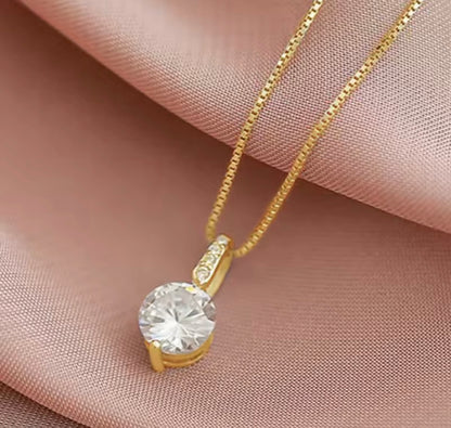 A gold chain necklace with a round clear gemstone pendant, displayed on draped pink satin fabric.