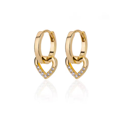 
A pair of gold huggie hoop earrings with interlocking heart designs, featuring a pavé diamond heart at the bottom of each earring, set against a clean white background with a soft reflection.